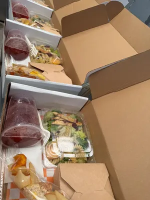 Cajas de cartón con comida, son cajas de box lunch, están sobre una mesa y tiene comida adentro