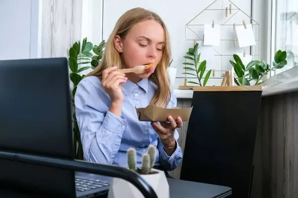 En una oficina está una mujer que está disfrutando de su box lunch, está sentada 