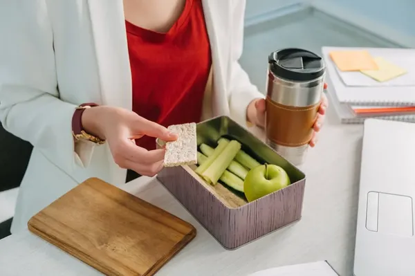 Un box lunch que está siendo comido por una mujer, ella está sentada y toma un café 
