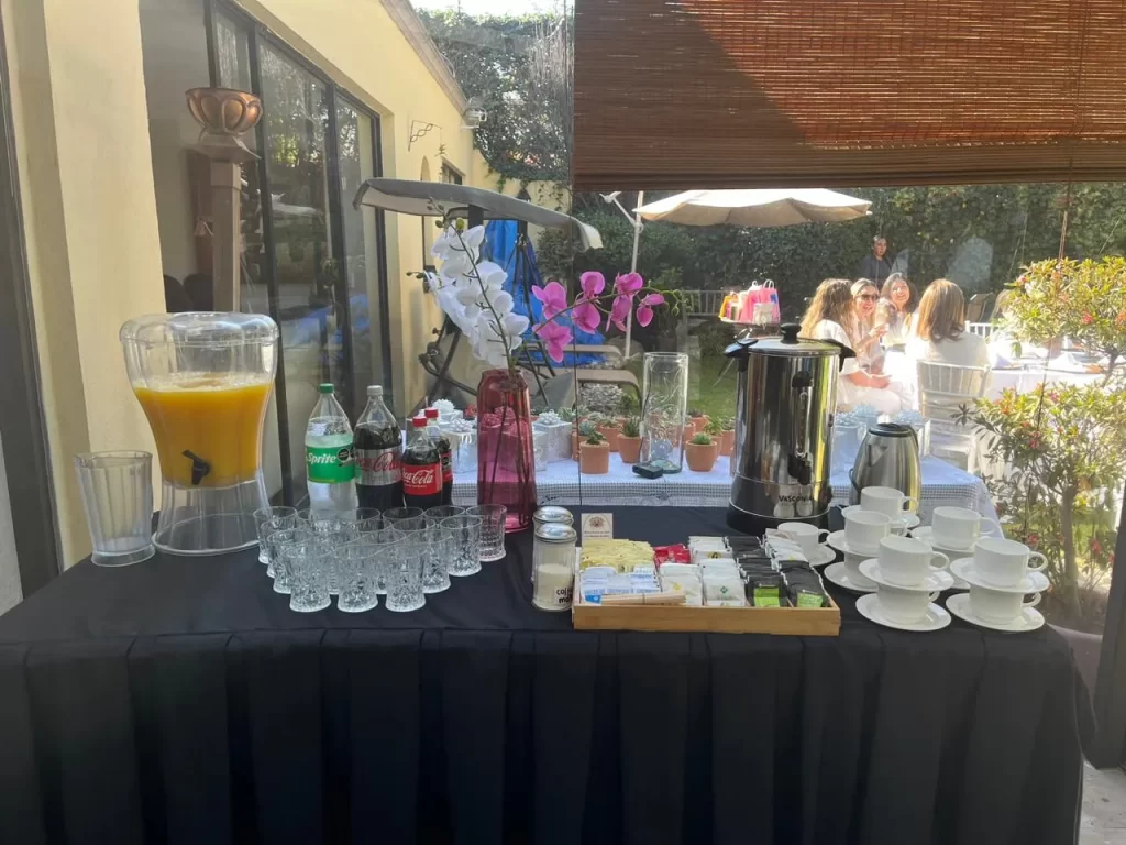 Un extenso coffee break montado al aire libre, bajo la luz del sol, sobre una mesa con mantel blanco.