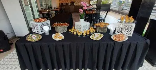 Mesa de recepción con una orquídea decorativa, bandejas de canapés y postres, y personas conversando en el fondo. Especialistas en servicios de banquetes corporativos
