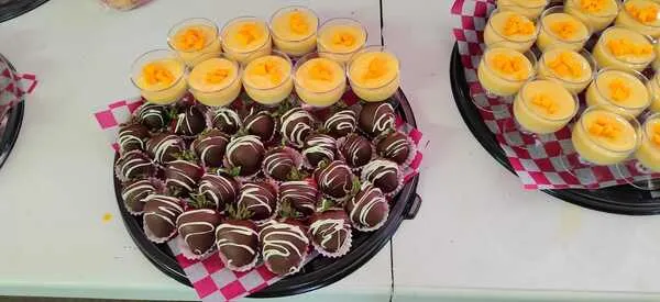Catering para eventos: Bandeja de deliciosas fresas bañadas en chocolate con glaseado blanco y vasitos individuales de postre de mango, perfectos para cualquier celebración.