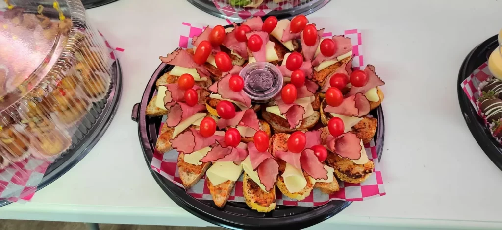 Bocadillos para fiestas tipo crostini con jamón, queso y tomate cherry servidos con dip central.