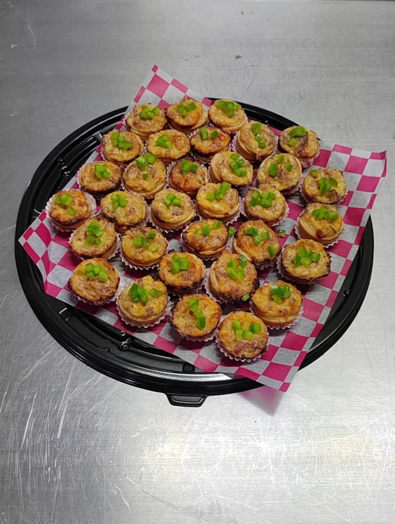Charola de mini quiches con pimiento verde, ideales como bocadillos para fiestas y reuniones.