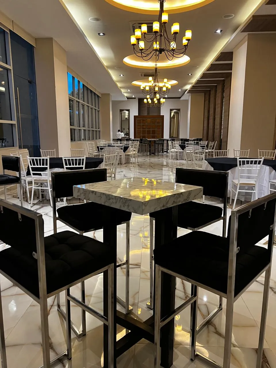 Mobiliario para eventos de lujo con mesas de mármol y sillas periqueras negras en un salón con iluminación elegante.
