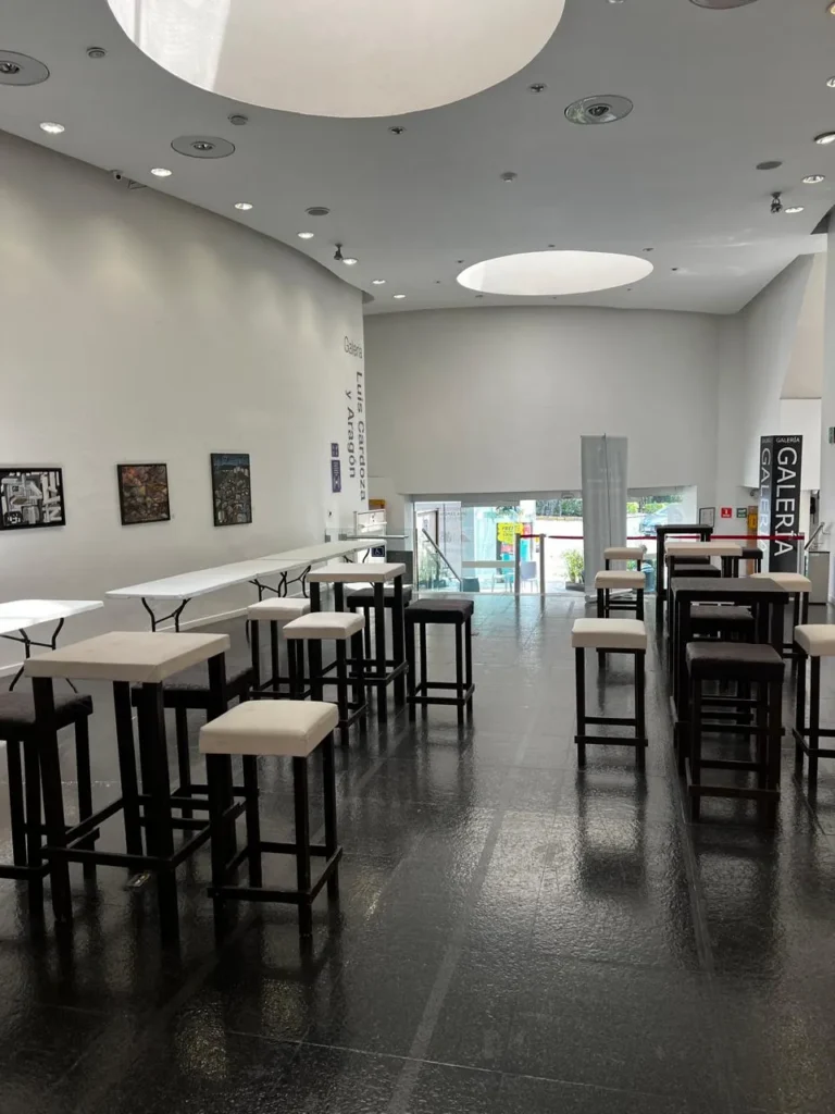Mobiliario para eventos tipo cóctel en una galería de arte, con bancos altos blancos y negros de diseño minimalista.