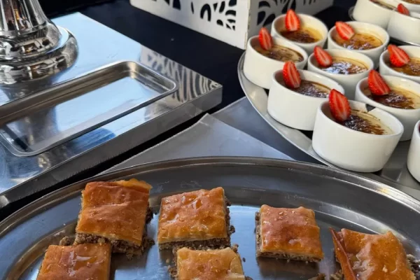 Hay unas bandejas con comida, hay centros de mesa blancos, todo adornado para banquetes para eventos empresariales