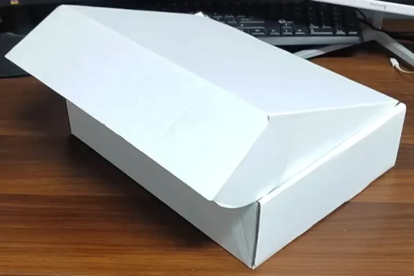 Caja lista para un box lunch a domicilio, está en una mesa de madera, la caja es blanca y está medio cerrada