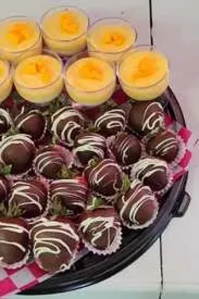 Catering para eventos: Bandeja de deliciosas fresas bañadas en chocolate con glaseado blanco y vasitos individuales de postre de mango, perfectos para cualquier celebración.