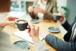 Personas en una oficina compartiendo café en tazas de cerámica durante un servicio de coffee break formal.