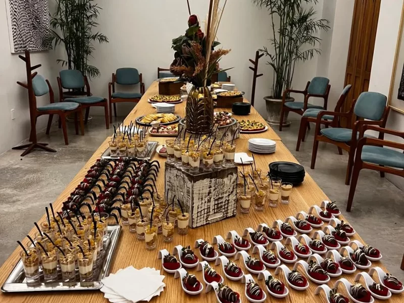 Una mesa que está llena de comida, hay bandejas y está acomodada con los servicios de banquetes