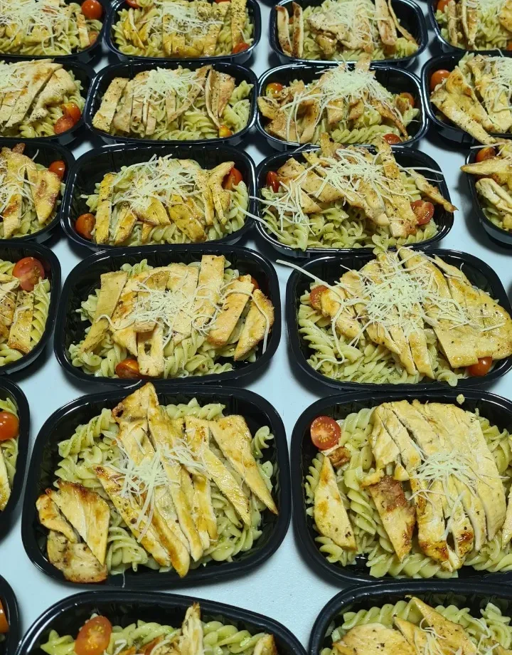 Variedad de menú saludable de box lunch para empresas con pasta fusilli al pesto, pollo a la plancha y tomates cherry.